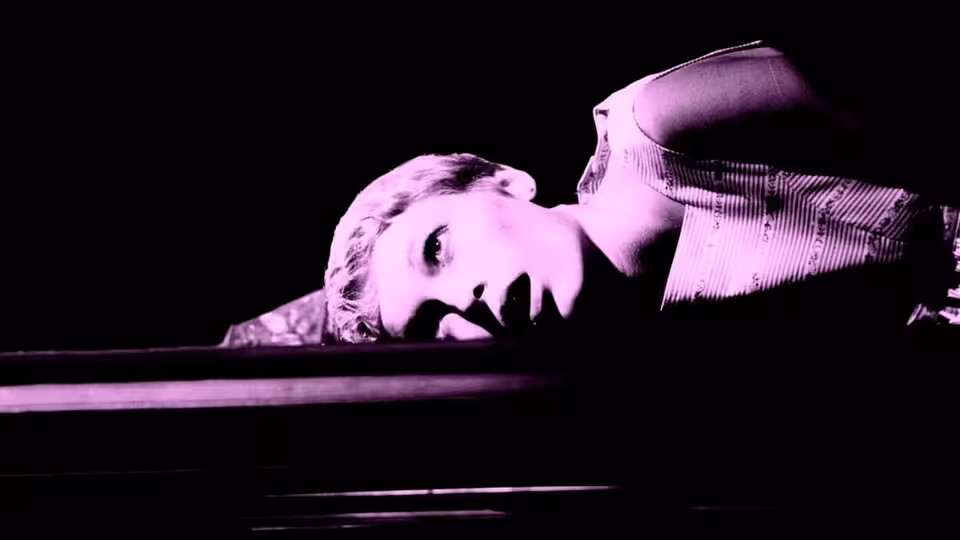 A woman peers over the edge of a dark piece of furniture