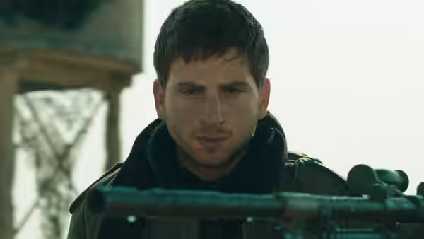 a young man with a rifle stares ahead in close-up