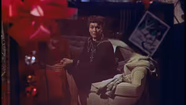 Sara Warren (Agnes Moorehead) stands beside an armchair in a dim living room