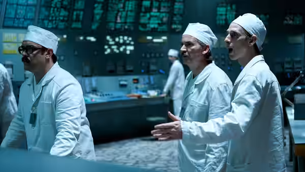 technicians in lab coats and caps standing before glowing control panels