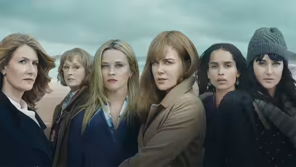Six women standing side by side on a beach under overcast skies