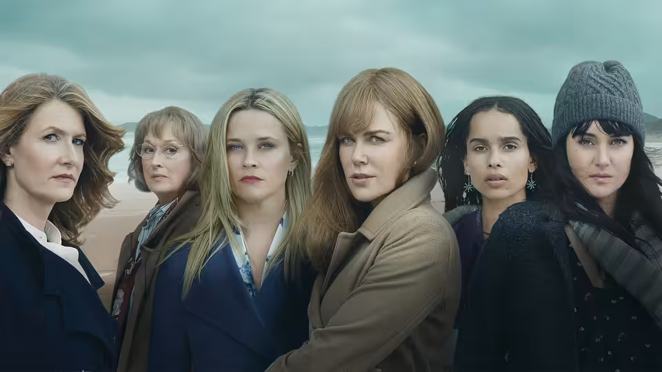 Six women standing side by side on a beach under overcast skies