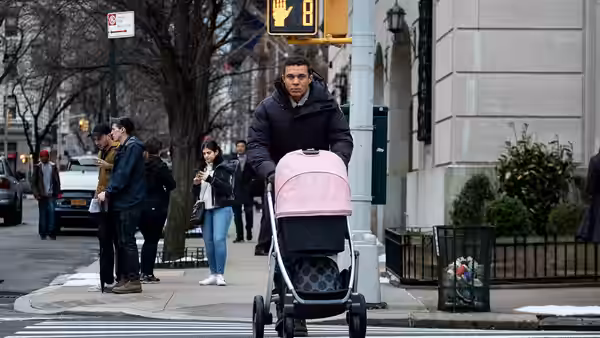 a man pushes a pink stroller across a city crosswalk