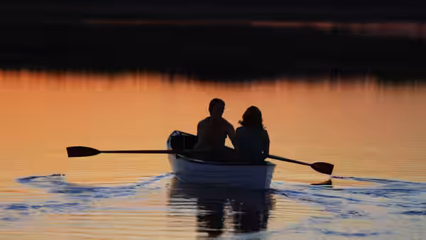 a couple sitting together in a rowboat on water at sunset