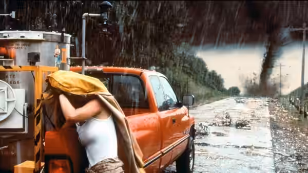 Jo (Helen Hunt) shelters beneath a tarp beside a red pickup as a tornado approaches