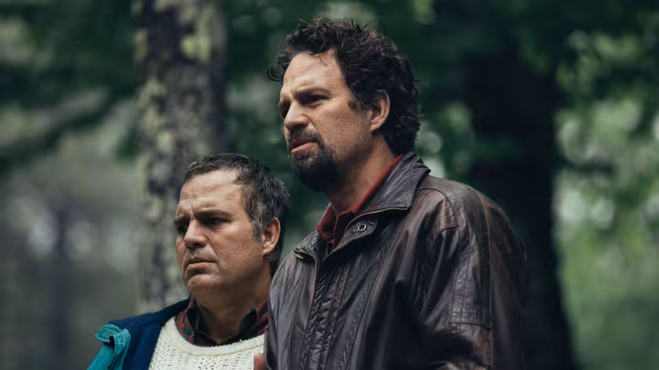 Two men standing among trees in a forest looking ahead intently