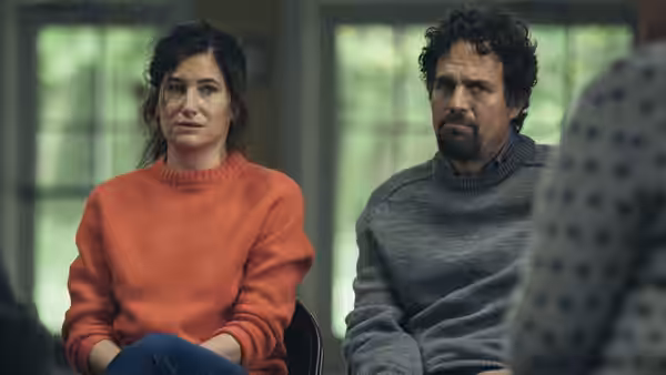 Woman in orange sweater seated beside Mark Ruffalo indoors