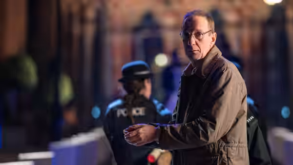 Christopher Edwards (David Thewlis) standing at night with police officers behind him