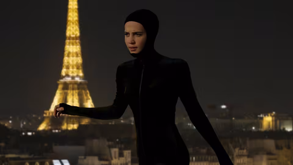 Mira (Alicia Vikander) standing with arm extended before the Eiffel Tower at night