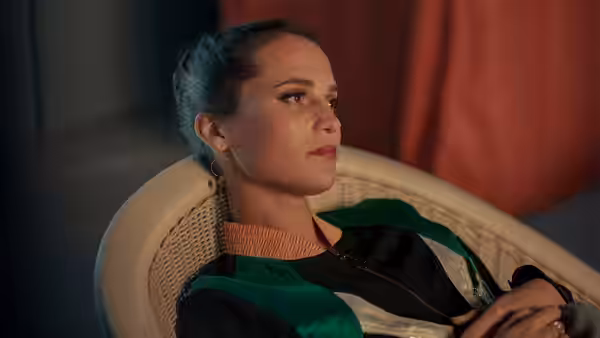 Mira (Alicia Vikander) reclining in a wicker chair gazing to the side