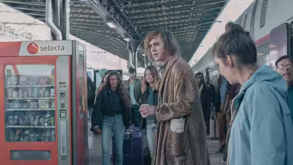 Woman in leopard-print coat holding coffee on crowded train platform