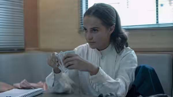 Mira (Alicia Vikander) examining playing cards while seated at a table