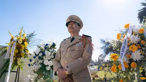 Man in military uniform standing among floral wreaths outside