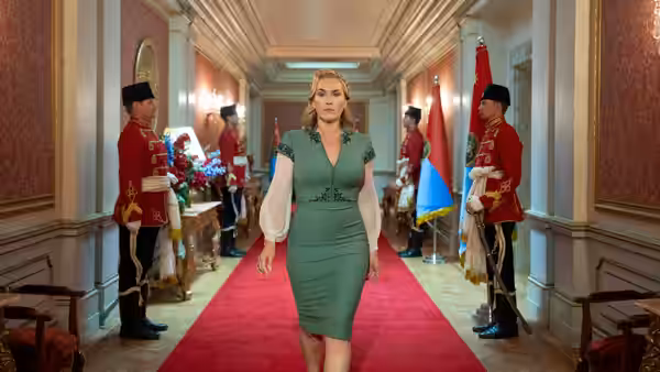 Chancellor Elena Vernham (Kate Winslet) walking down a red carpet past uniformed guards