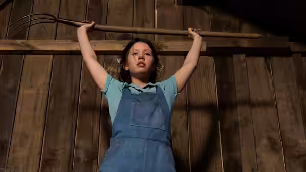 Pearl (Mia Goth) lifting a rake inside a barn