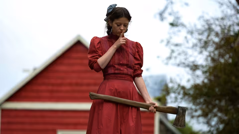 Pearl (Mia Goth) holding an axe outside a red barn