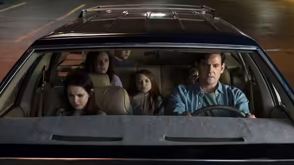 A man drives a car at night with children in the back