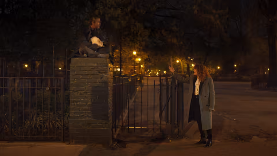 Nadia (Natasha Lyonne) gesturing toward a man perched on a brick pillar at night