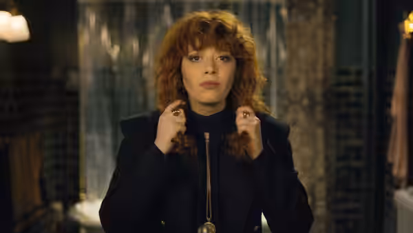 Nadia (Natasha Lyonne) adjusting her curly hair while wearing gold rings
