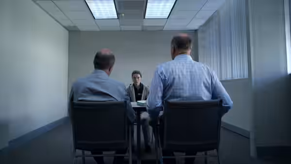 Marie Adler (Kaitlyn Dever) sits facing two men at a table in a small room