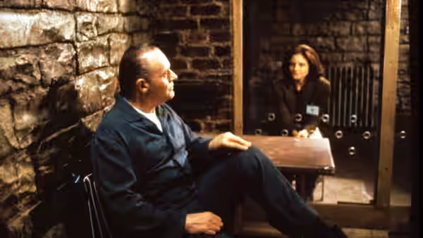 Dr. Hannibal Lecter (Anthony Hopkins) seated in his cell as Clarice Starling (Jodie Foster) watches