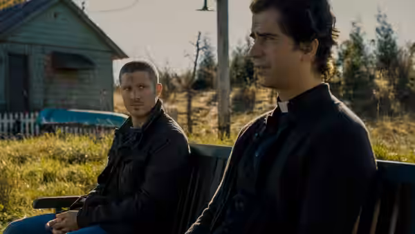 Riley Flynn (Zach Gilford) and Father Paul Hill (Hamish Linklater) seated on a bench outside