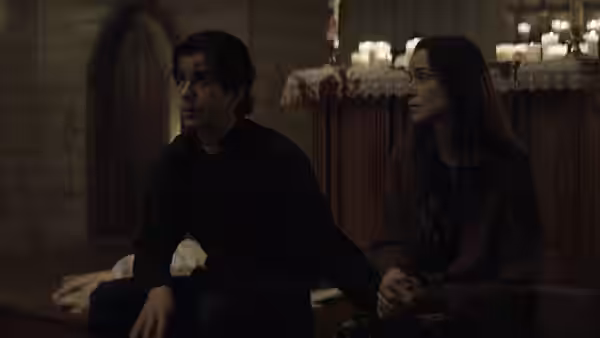 Father Paul Hill (Hamish Linklater) sitting with a woman in a church pew