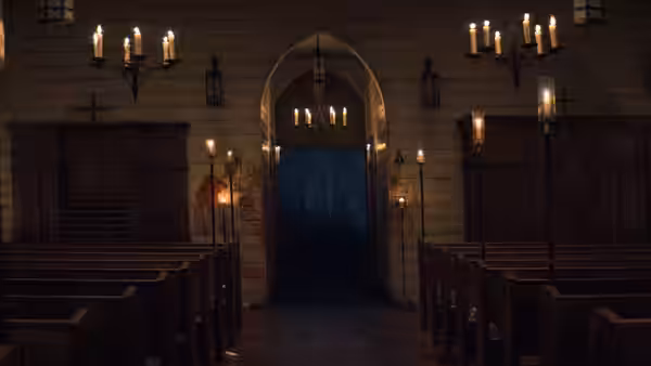 Empty wooden church interior with lit candles and an open rear door