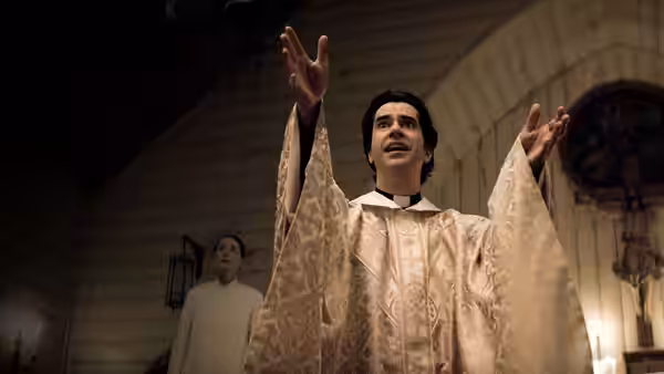 Father Paul Hill (Hamish Linklater) raising both arms while speaking in church