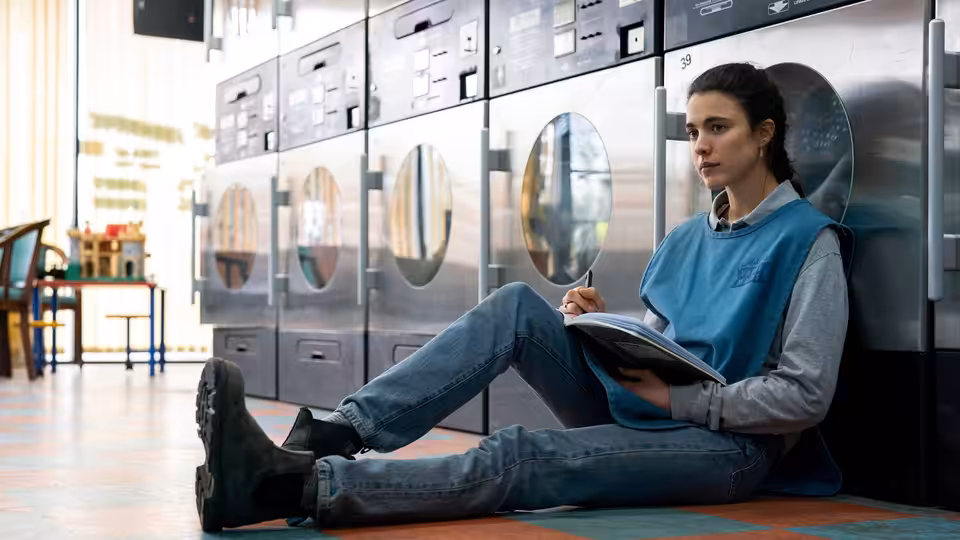 Alex (Margaret Qualley) sitting on the floor in a laundromat writing in a notebook