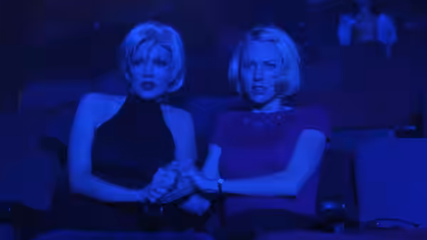 two blonde women holding hands while seated together in a dark theater