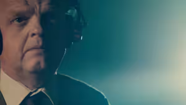 Gilderoy (Toby Jones) listens intently through large black headphones