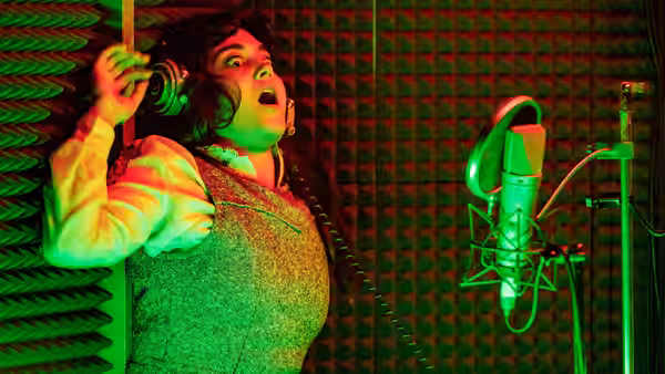 A woman leans against acoustic foam wearing headphones and singing
