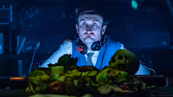 A man with headphones stares wide-eyed at a desk of produce