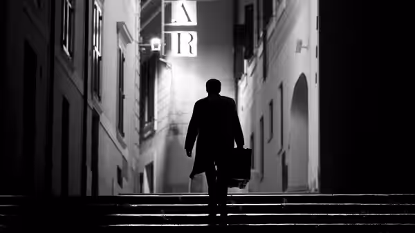 A man in a suit walks up steps carrying a briefcase at night