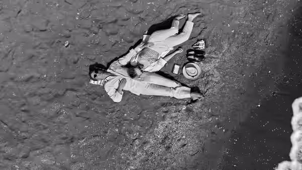 Two people lie on the sand with personal items scattered around them