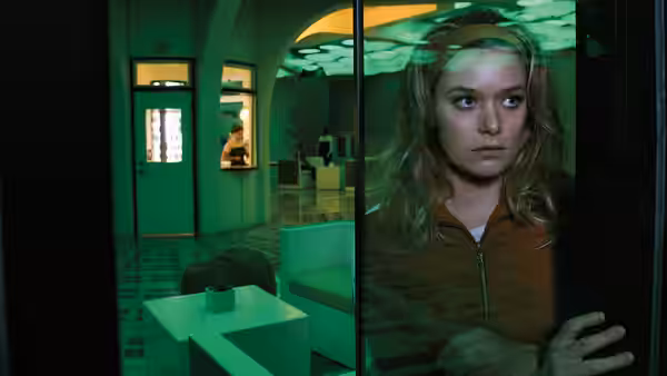 Sydney Barrett (Rachel Keller) peering through glass in a green room