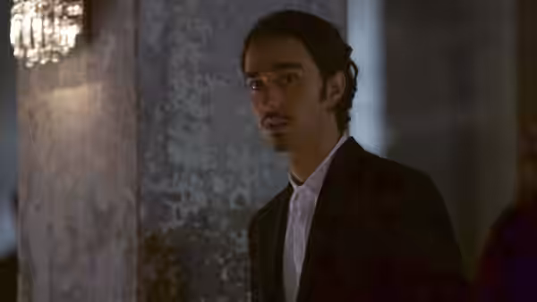 Amir (Alex Wolff) stands in a dark suit beside a textured wall