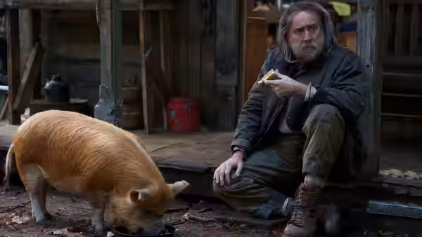 Rob Feld (Nicolas Cage) sits beside his pig outside a weathered woodland cabin