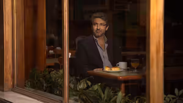 Man in suit sits at a table inside a cafe viewed through glass