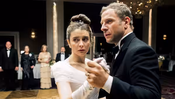 Bride in white gown and groom in tuxedo stand together in a ballroom