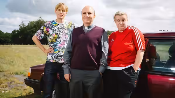 Reverend Seaton (Paul Chahidi) standing with Kerry and Kurtan by a maroon car
