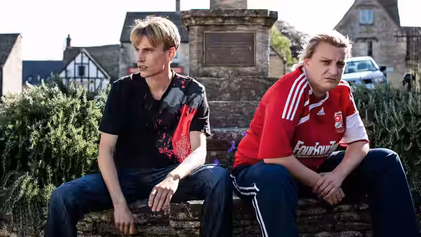 Kurtan (Charlie Cooper) and Kerry Mucklowe (Daisy May Cooper) seated on a stone wall