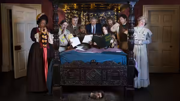 A group of ghosts stand around a four-poster bed with a severed head on the floor