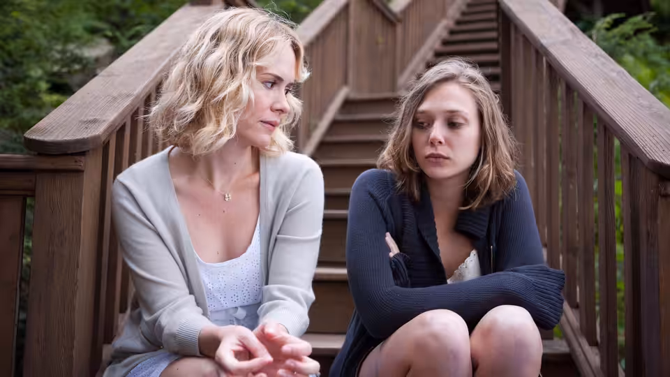 Martha (Elizabeth Olsen) and Lucy (Sarah Paulson) sit together on wooden stairs