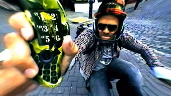 Man in helmet and sunglasses holds out green mobile phone while moving fast
