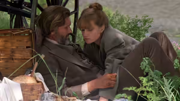 A bearded man and a woman in a gray coat lie together on the grass