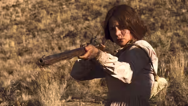 a woman aiming a long rifle across dry grassy terrain