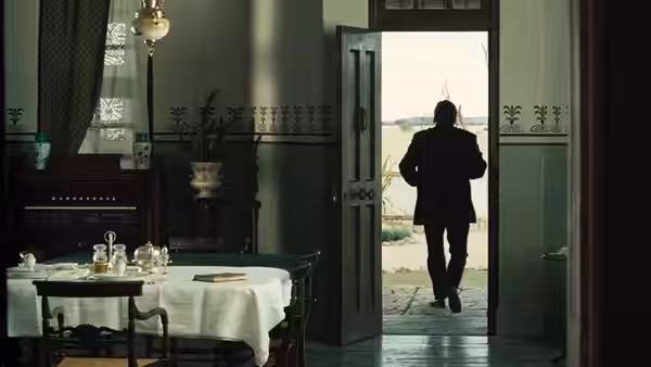 A man walks through an open doorway from a furnished dining room
