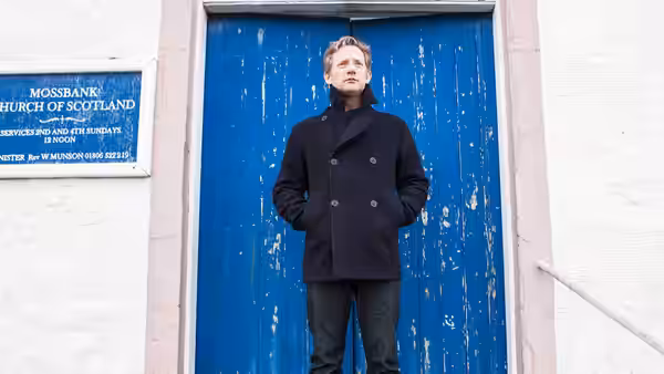 Duncan Hunter (Mark Bonnar) standing before a blue wooden door